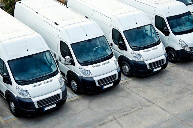 4 white vans in a row in a car park or compound
