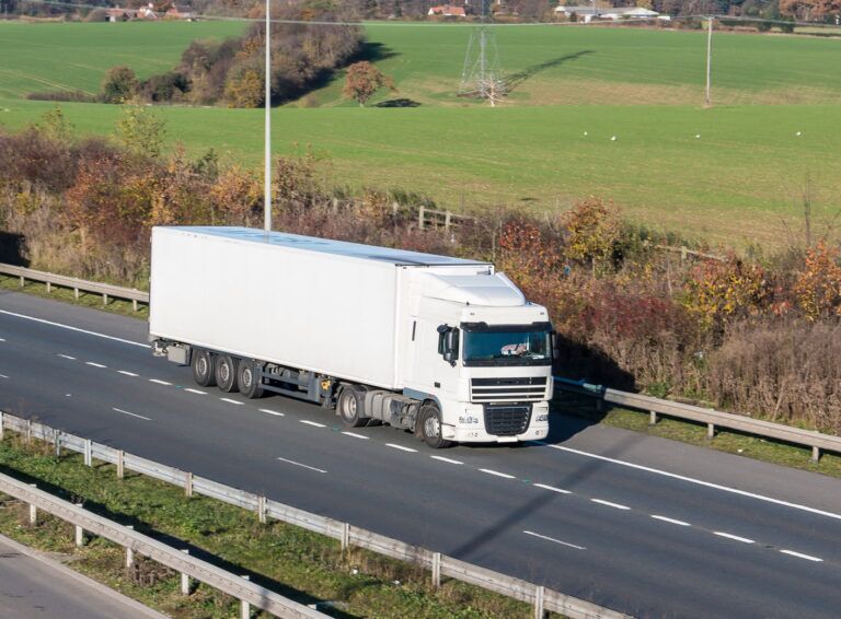 A white lorry driving on a motorway with green fields in the background