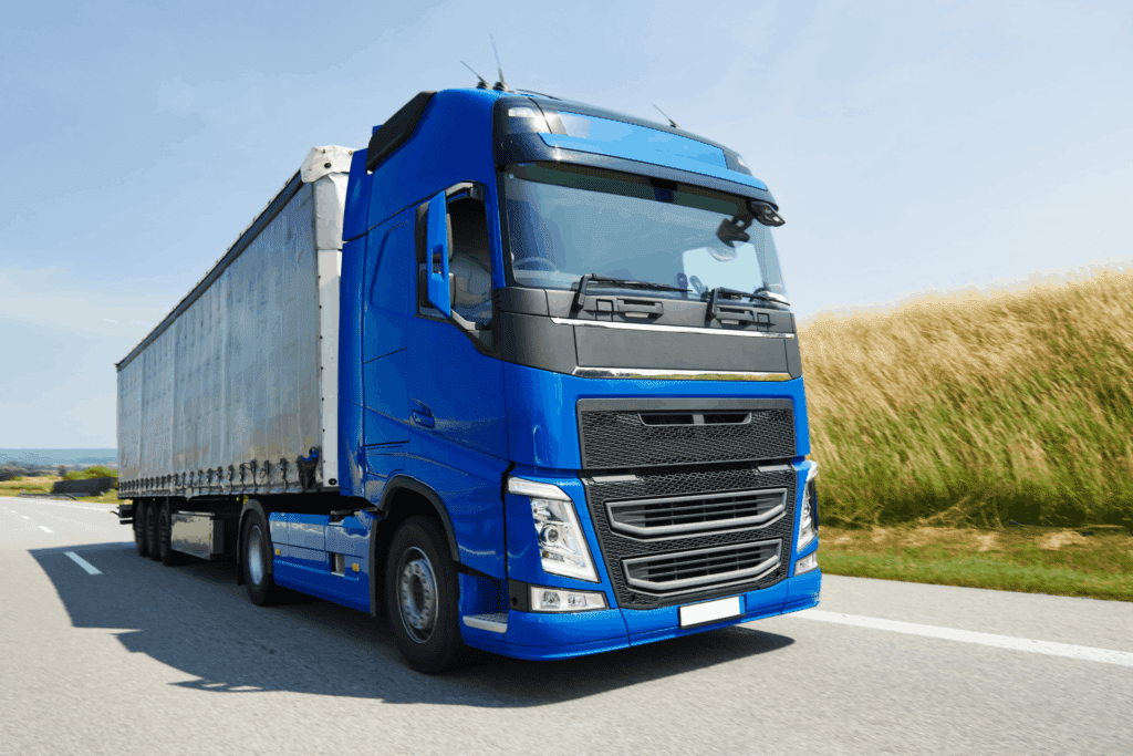 A lorry with a blue tractor unit, also known as the drivers cab, driving on a road with wheat fields in the background