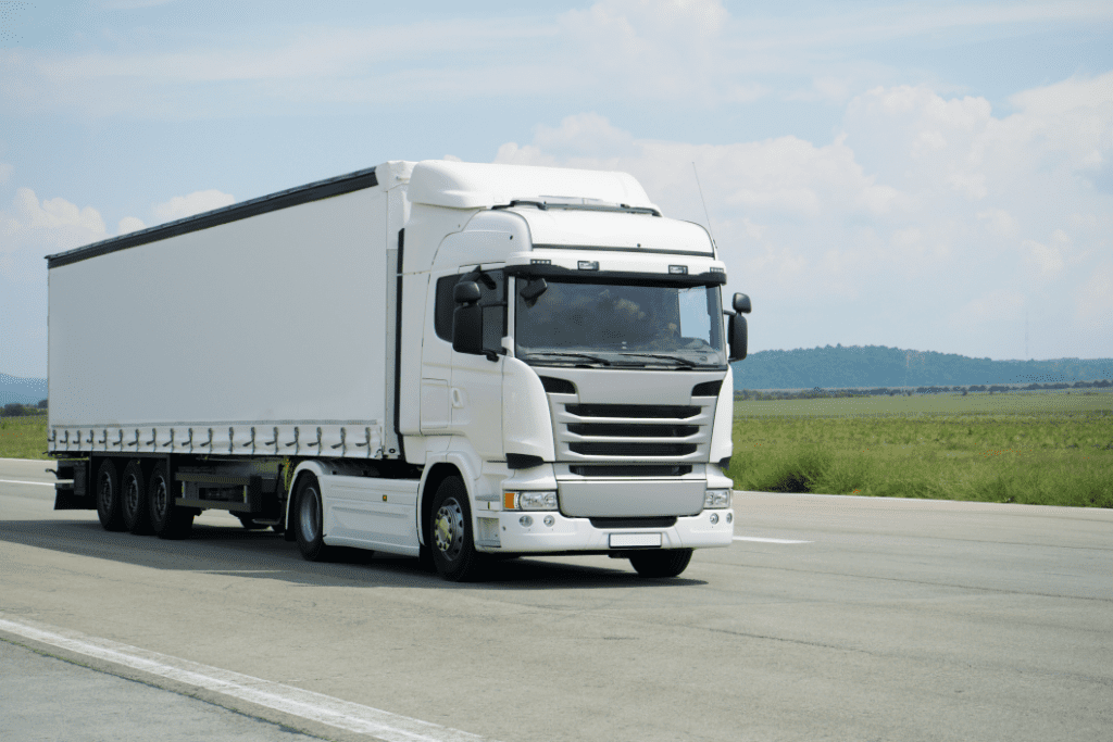 a white lorry on the road with a field behind and a mountain in the distance